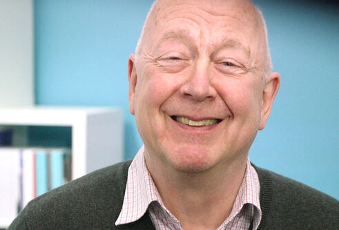Older man looking directly at the camera and smiling, with a light blue background