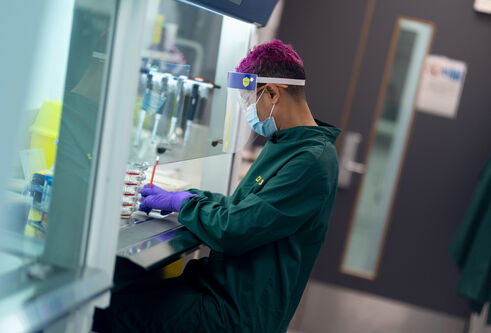 Person in green boiler suit facing left, working at scientific piece of equipment