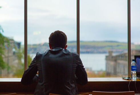 A student looks out of the window of DUSA, looking across the Tay to Fife.