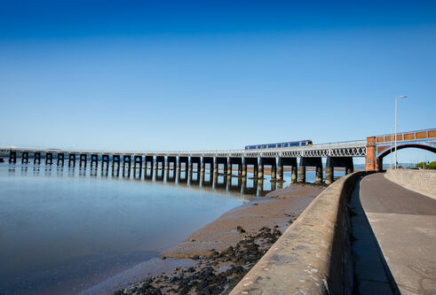 Train crossing bridge over River Tay against bright blue sky