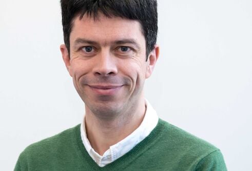 man with dark hair wearing a white shirt and green jumper