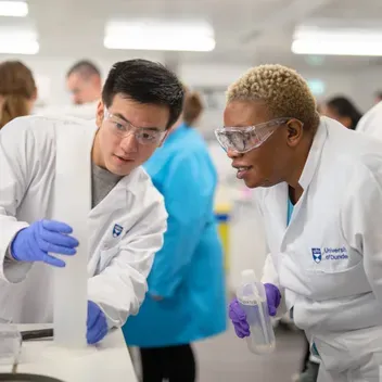 Two students with white lab coats on conducting an experiment in a lab at Dundee
