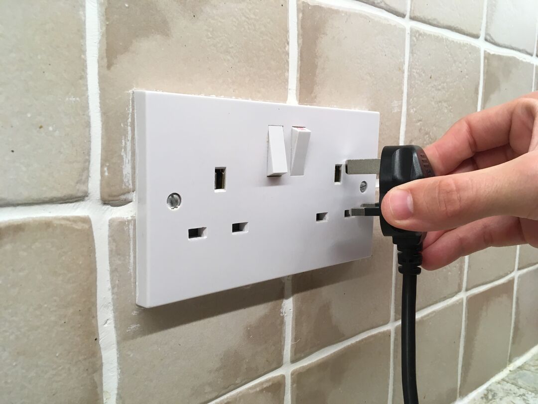 Photograph of a hand holding a UK plug next to a UK power socket