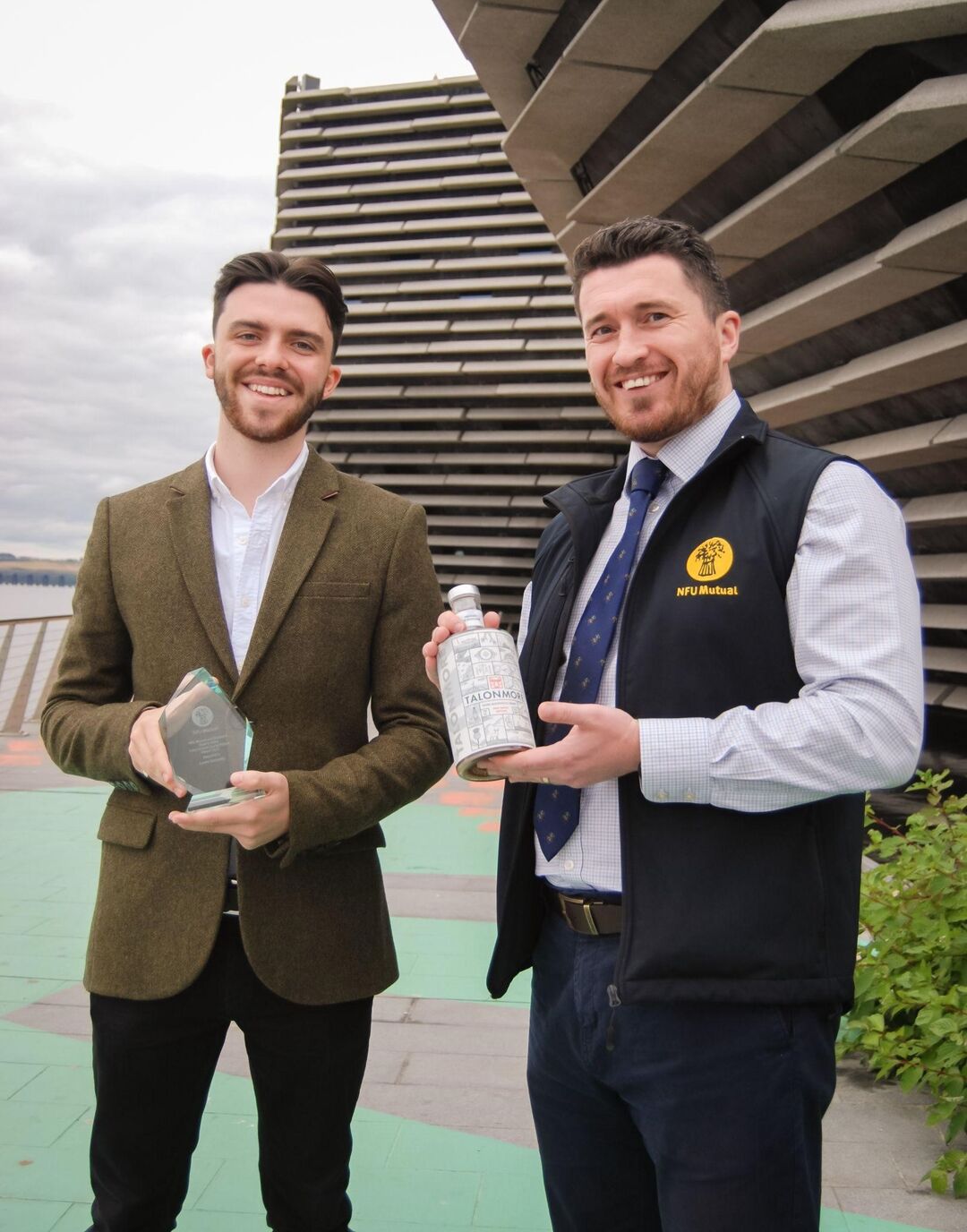 Lewis Kennedy holding an award, with Sean Mochan holding a bottle of gin outside the V&A Dundee